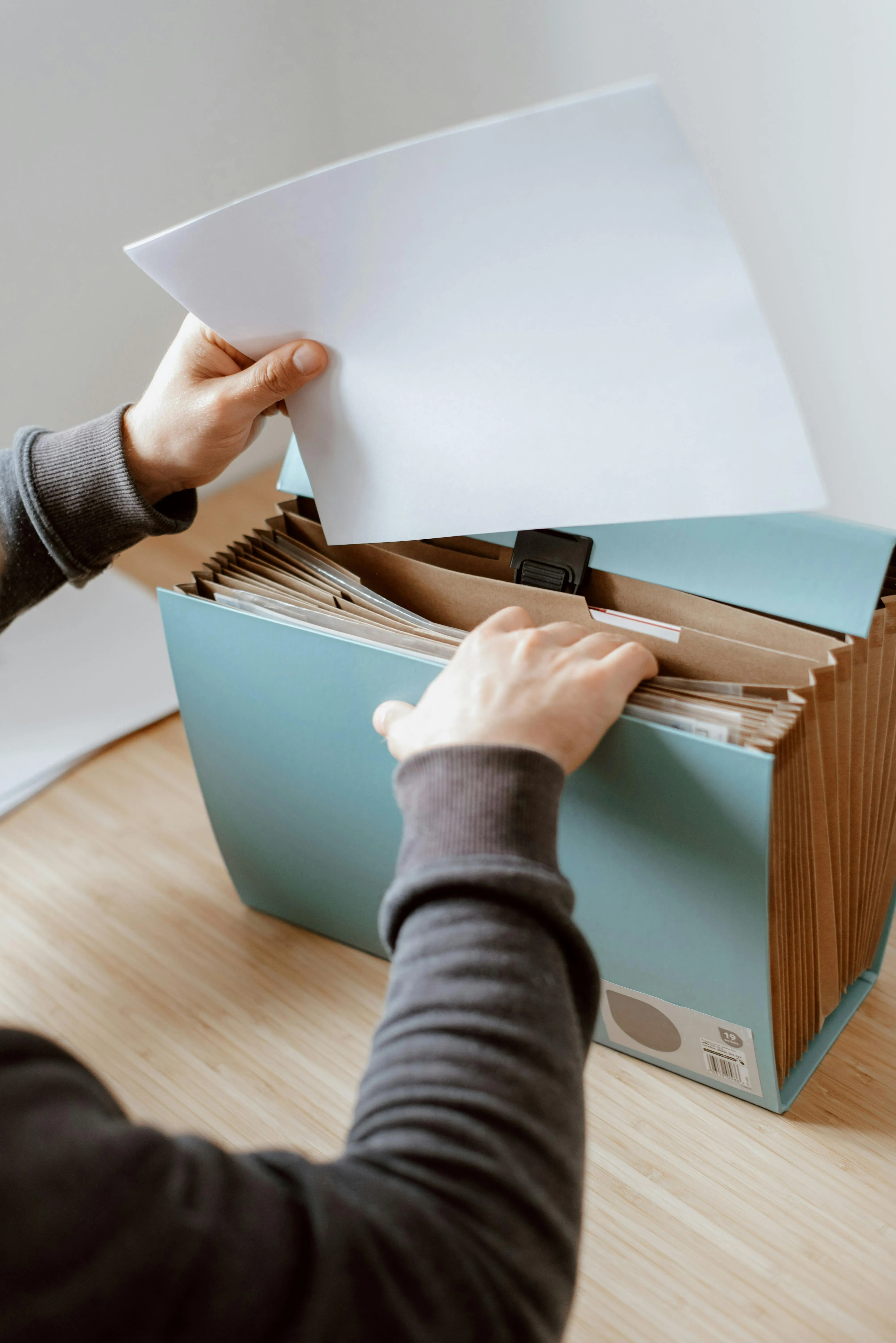 A person filing documents into a big paper multi-folder.